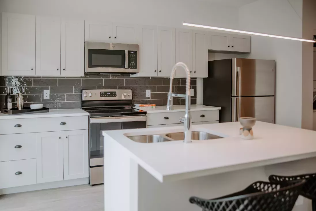A modern kitchen in Industry Columbus Apartments featuring sleek white cabinetry, stainless steel appliances, and a stylish island with a dual sink and high-arc faucet.