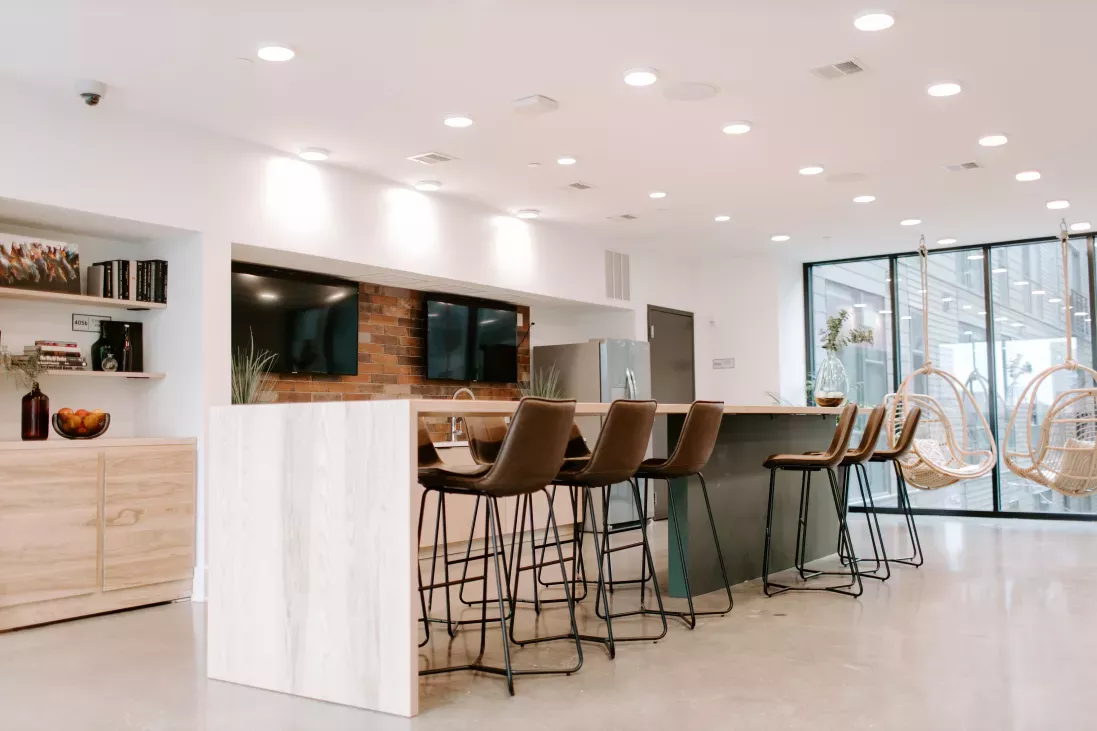 A spacious and well-lit community lounge in Industry Columbus Apartments, featuring high-top seating, hanging wicker chairs, and a kitchenette with modern finishes.