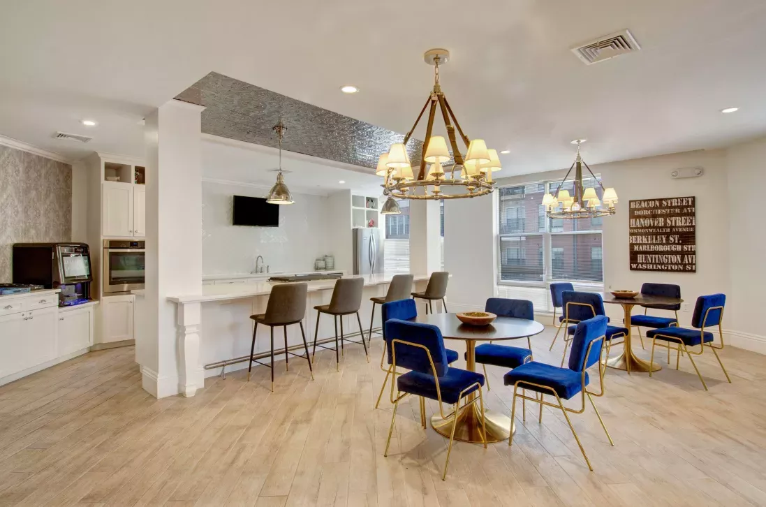 Modern community kitchen and dining space with pendant lighting, navy chairs, and light wood flooring.