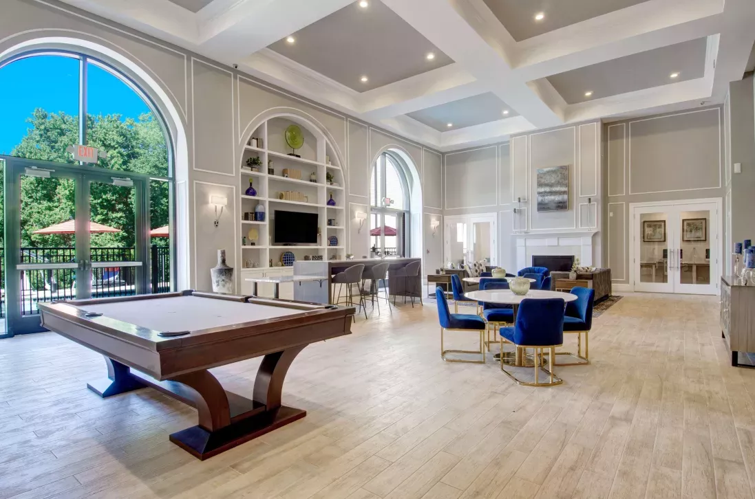 Spacious resident lounge featuring pool table, tall arched windows, and built-in shelving with decor.