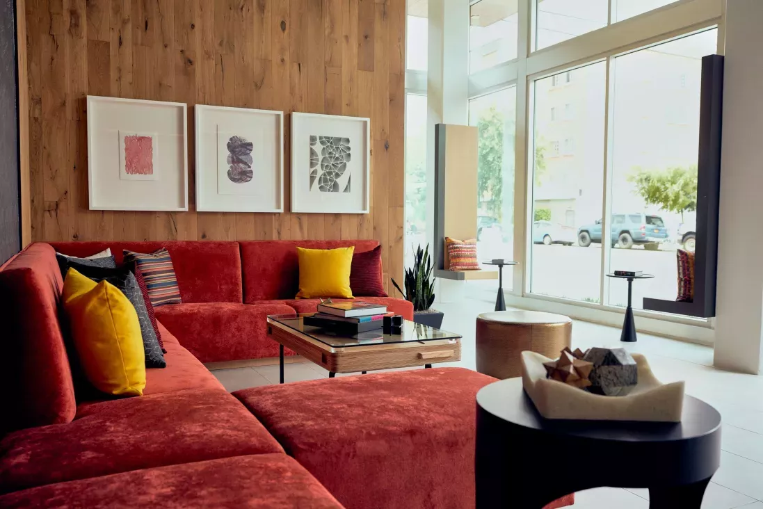 Contemporary resident lounge featuring a red sectional sofa, large windows, wood accent wall, and colorful artwork.