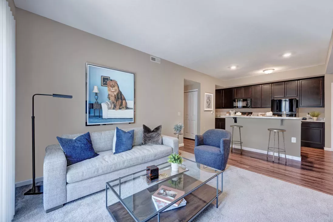 Open-concept living space with a contemporary sofa, large lion artwork, and a view into a kitchen with dark cabinetry and a breakfast bar.