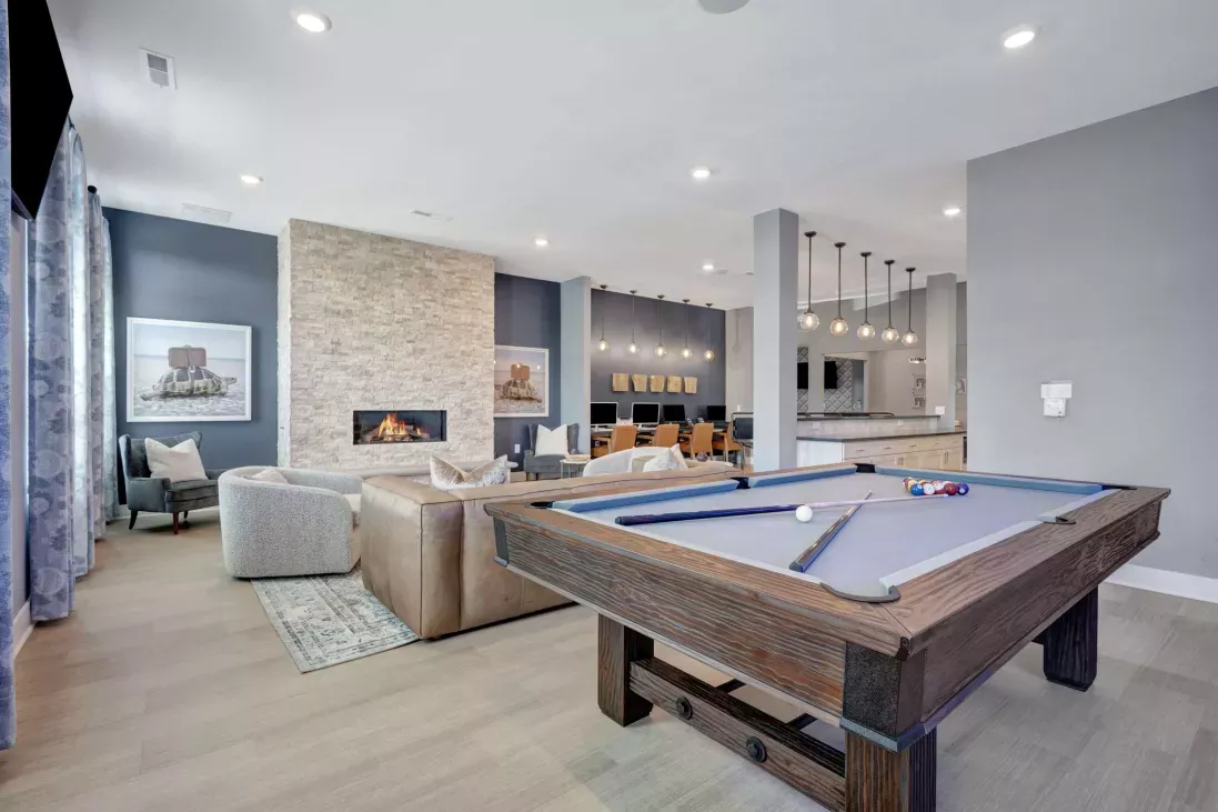 Amenity space with a pool table, resident lounge seating, and a business center, accented by modern lighting and a stone fireplace.