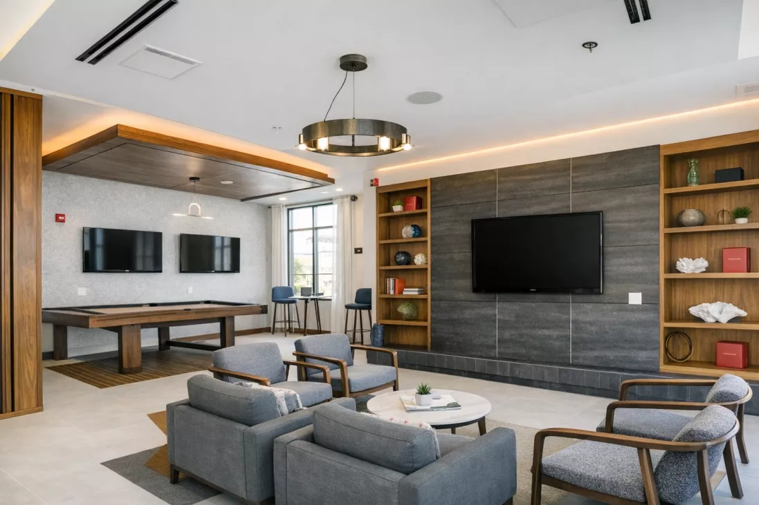 Contemporary common room featuring a billiards table, lounge seating, and a TV on a dark stone accent wall with bookshelves.