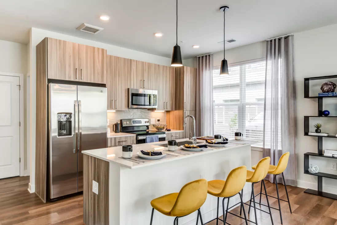 Modern kitchen with light wood cabinets, stainless steel appliances, a white island, and three yellow bar stools.