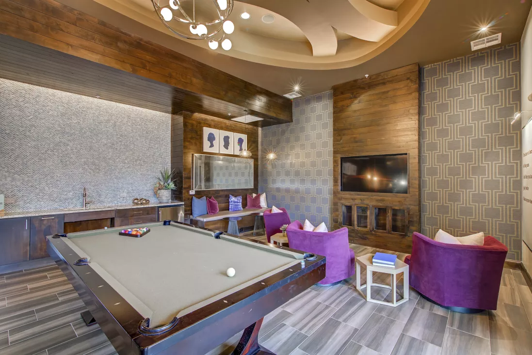 Luxurious lounge with a pool table, plush purple seating, wall-mounted TV, and elegant lighting.