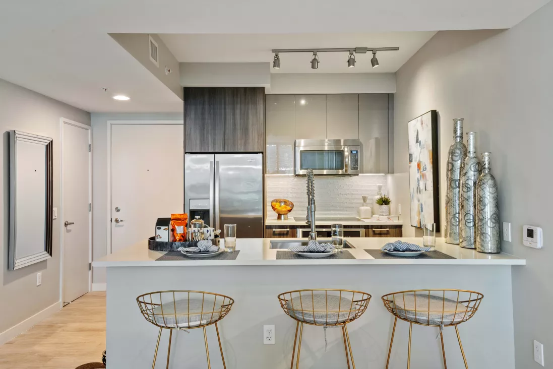 Modern kitchen featuring an island with three gold wire bar stools, light grey cabinets, and stainless steel appliances.