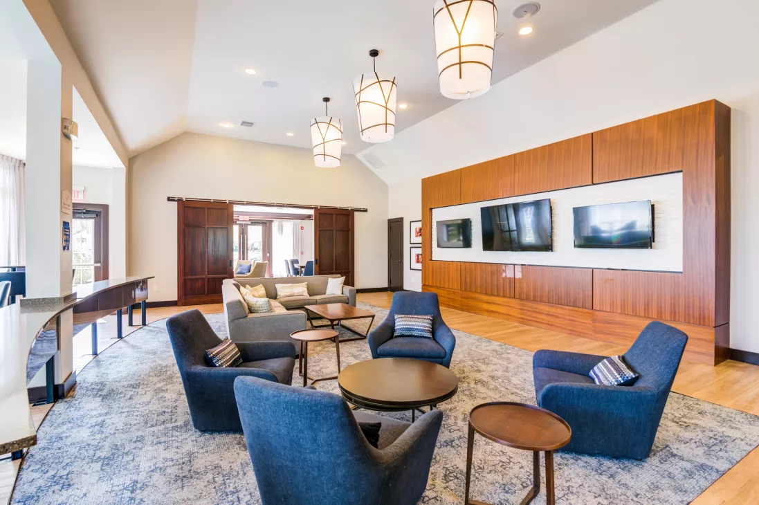 Spacious common area with modern blue seating, patterned rug, and a media wall with three televisions.