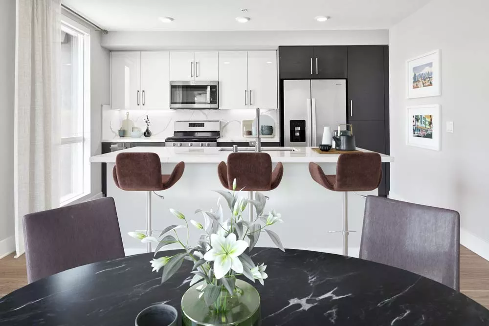 Modern apartment kitchen and dining area with white cabinets, stainless steel appliances, island seating, and a black marble dining table.