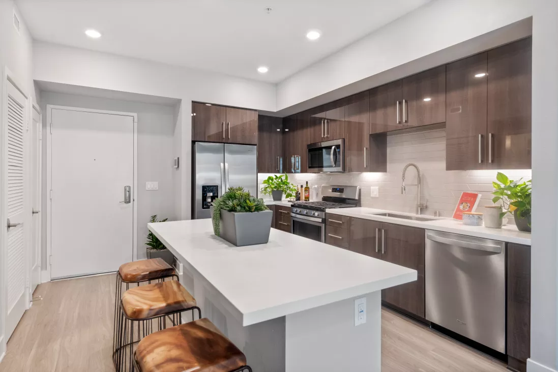 Modern kitchen with dark brown cabinets, stainless steel appliances, white island, and three wooden bar stools.