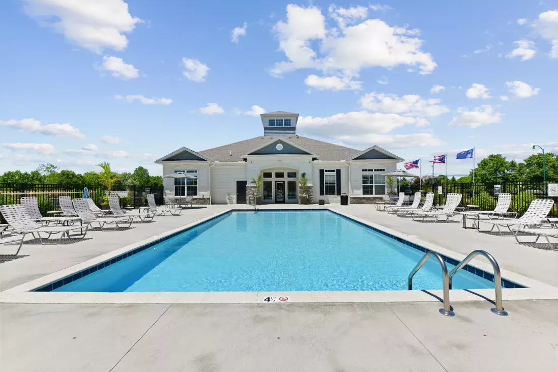 Outdoor swimming pool with white lounge chairs and a clubhouse under a blue sky.