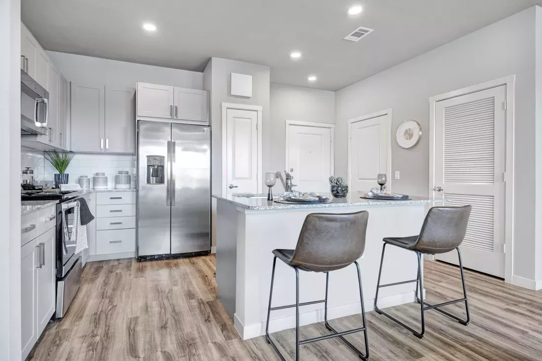Modern kitchen with light gray cabinets, stainless steel appliances, a center island with two bar stools, and wood floors.