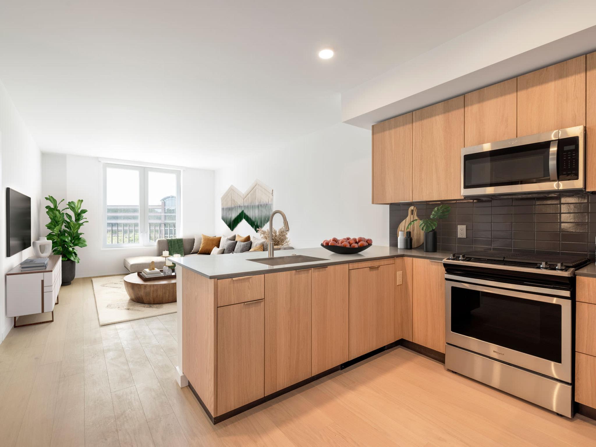 Modern kitchen featuring stainless steel appliances, wood cabinetry, and a sleek tile backsplash at The Edmund Apartments.