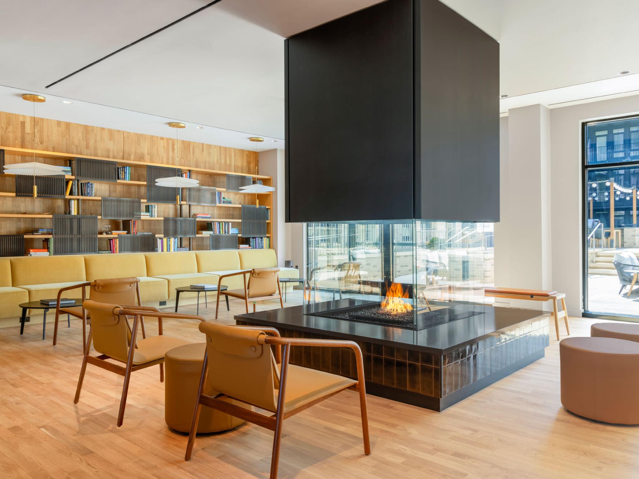 An inviting common area with a glass-encased central fireplace, ample seating, and an outdoor view, blending luxury and comfort for social gatherings.