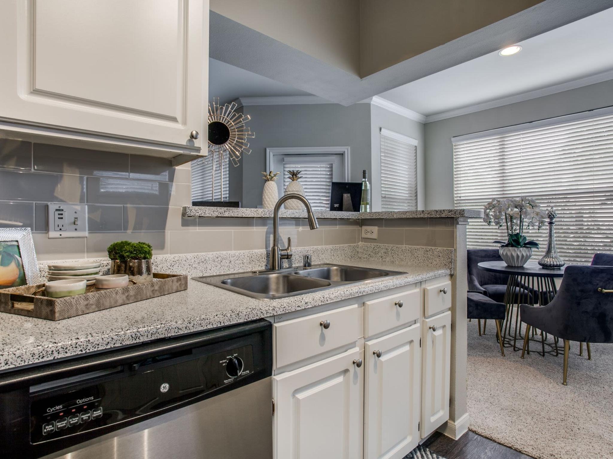 Modern kitchen with granite countertops, stainless steel appliances, and an open concept design leading into a brightly lit living room with large windows at Arboretum Estates.