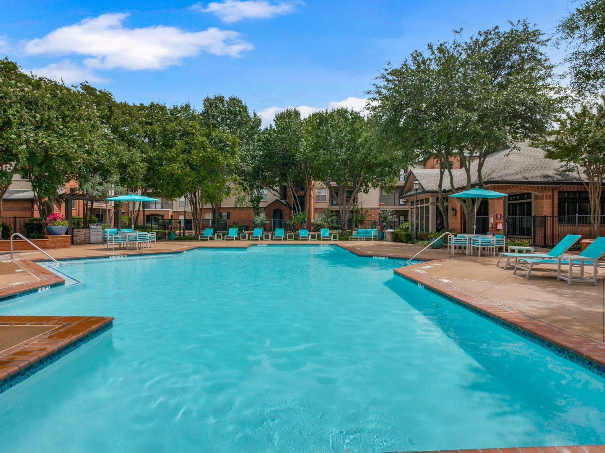Sparkling resort-style swimming pool surrounded by lounge chairs, umbrellas, and lush greenery, offering a relaxing retreat at Arboretum Estates.