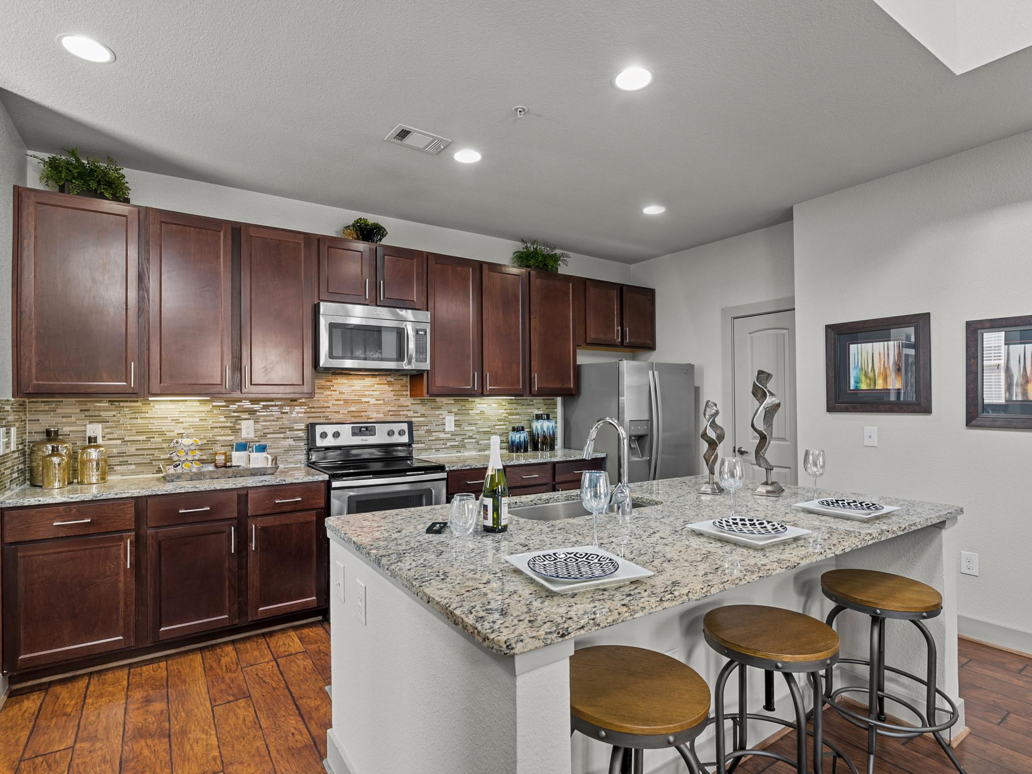 A modern kitchen with stainless steel appliances, dark wood cabinetry, granite countertops, and a large island with barstools.