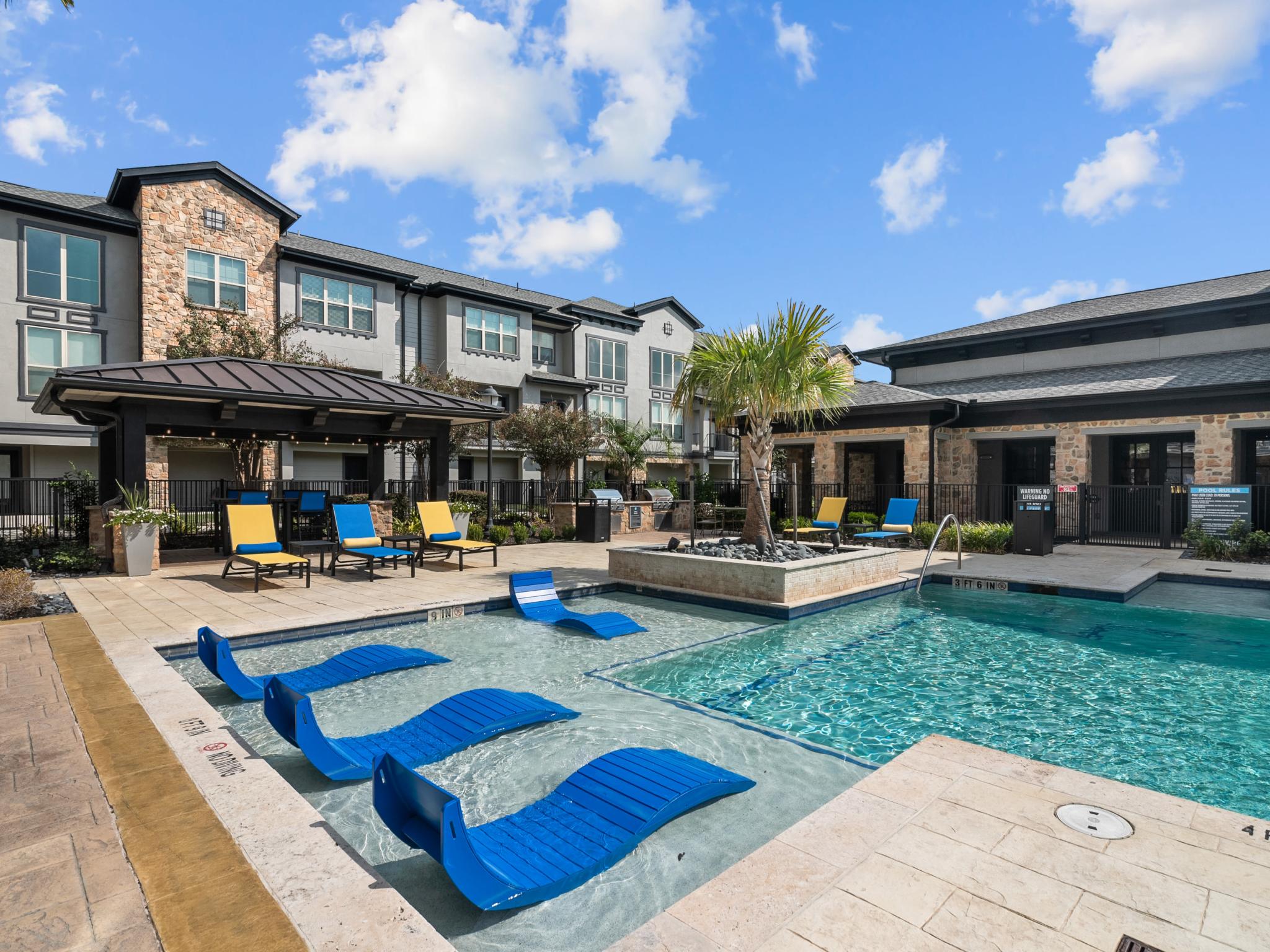 A luxurious outdoor pool area with blue lounge chairs, a shaded cabana, and resort-style landscaping.