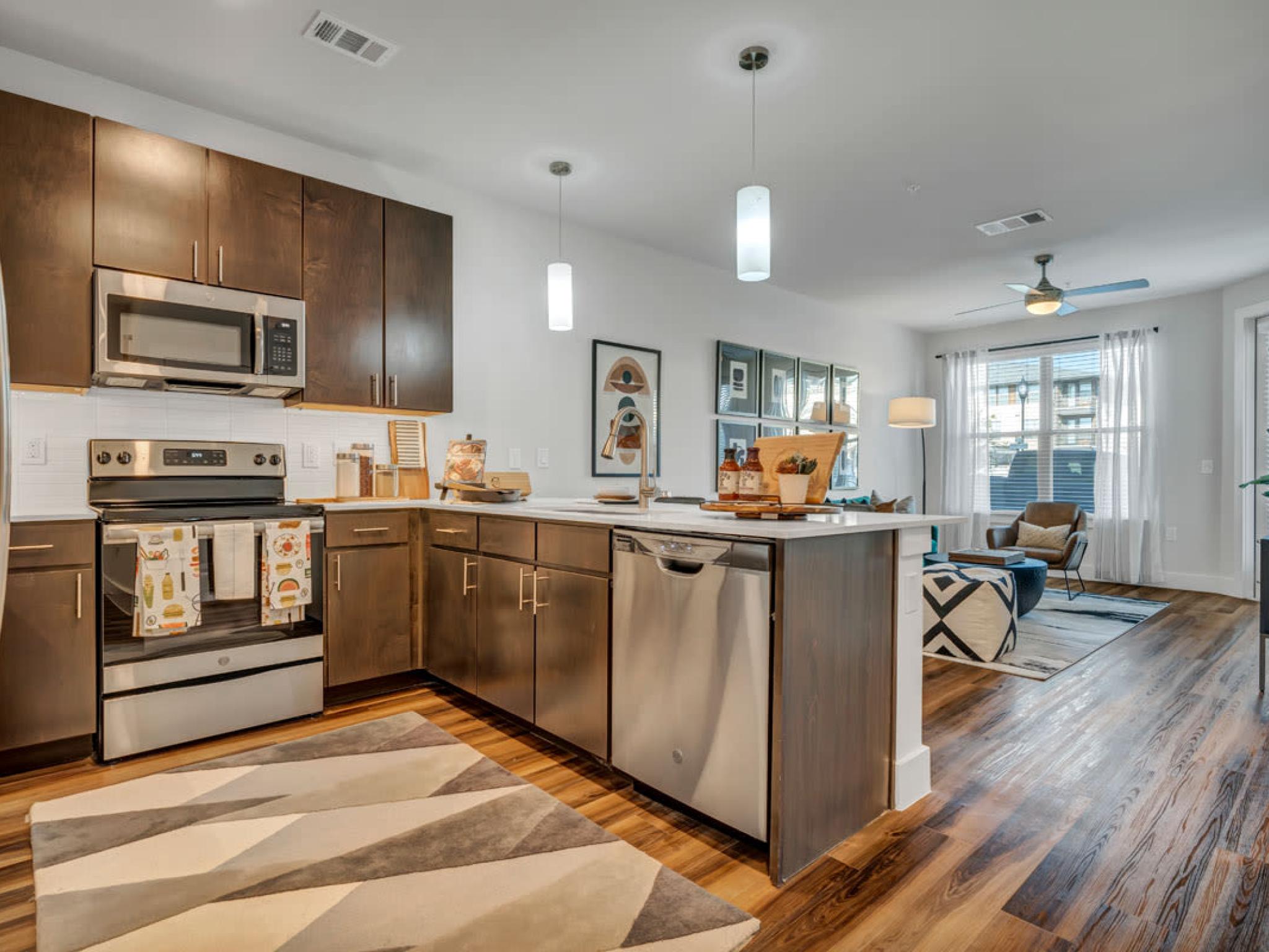 A modern kitchen with dark wood cabinets, stainless steel appliances, and a bright, open layout connecting to the living space.
