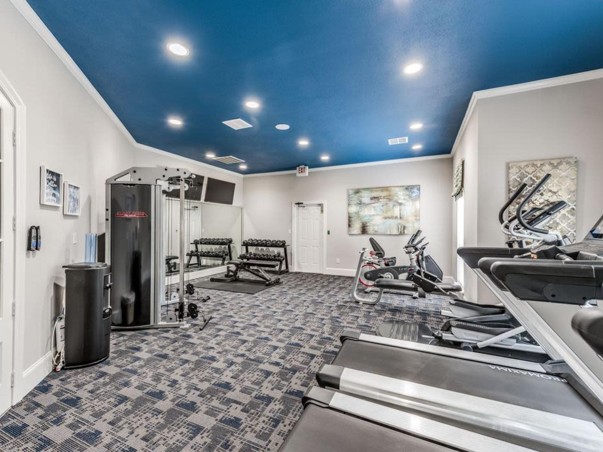 State-of-the-art fitness center at The Landings of Conroe Luxury Apartments, featuring modern exercise equipment and vibrant blue ceiling design.