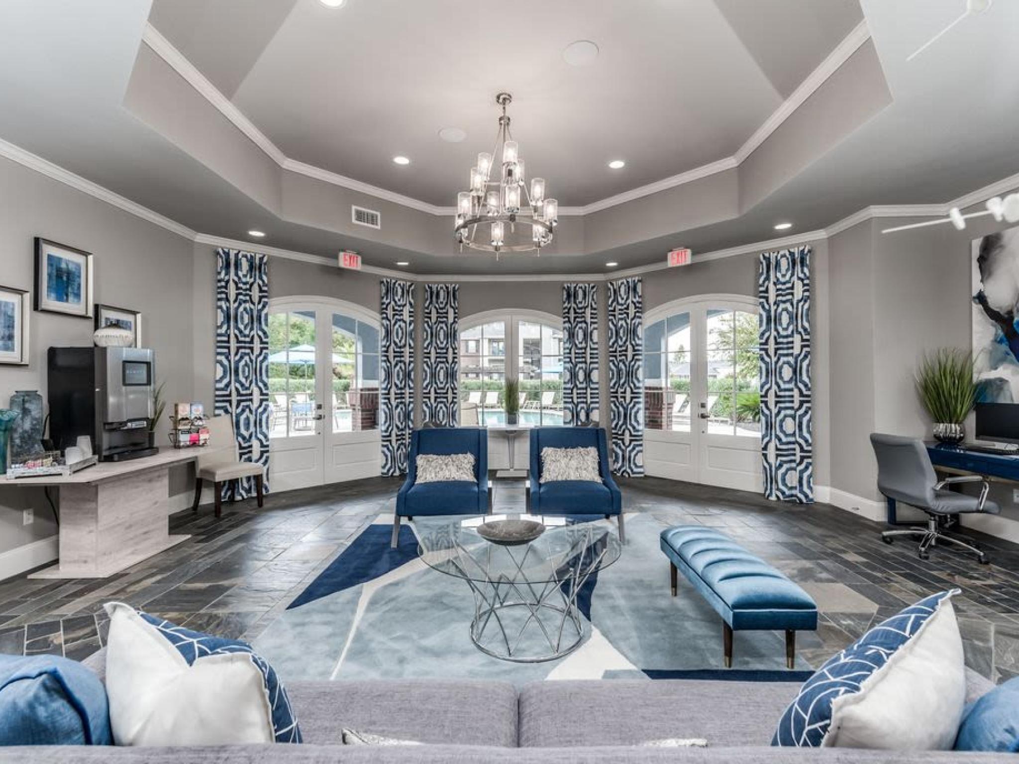 Elegant and inviting resident lounge with bold blue decor, a stunning chandelier, and access to the pool area at The Landings of Conroe.