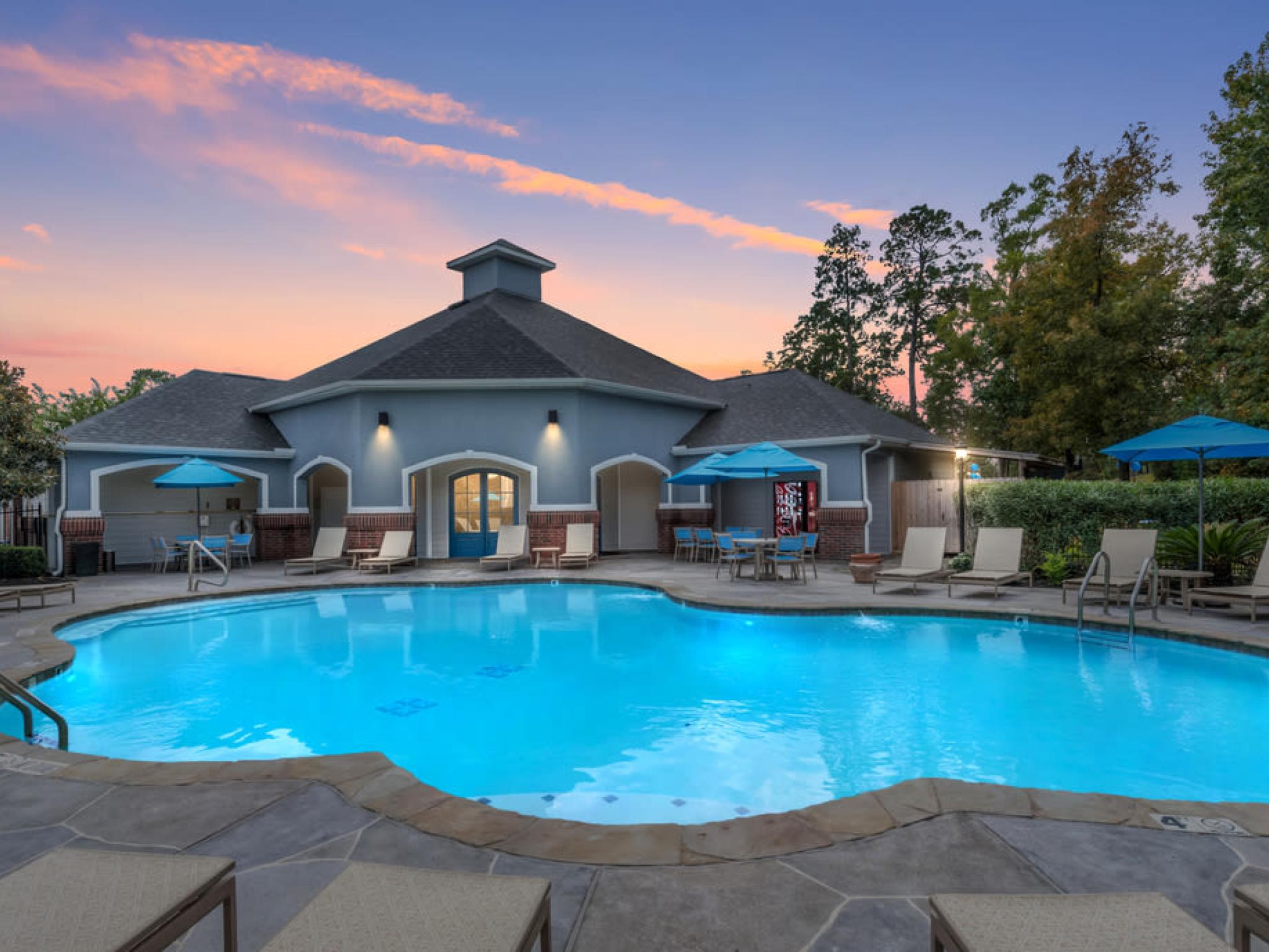 Resort-style pool at The Landings of Conroe Luxury Apartments with comfortable seating, umbrellas, and a serene evening ambiance.