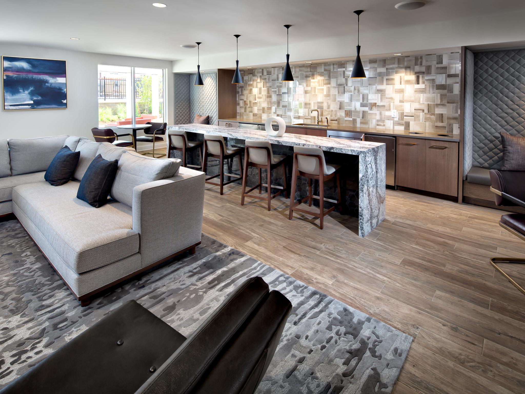 A stylish resident lounge with a sleek marble island, bar seating, cozy sectional sofa, and modern lighting at The Mark at Mamaroneck Luxury Apartments.