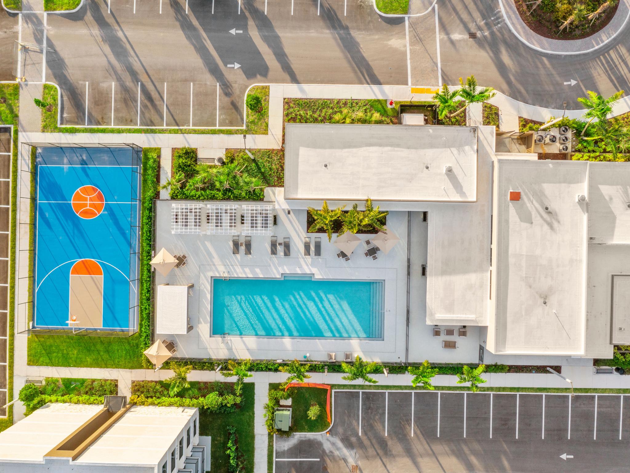 Aerial view of Pine Ridge Luxury Apartments showcasing a basketball court, a sparkling swimming pool, and lush landscaping surrounded by ample parking.