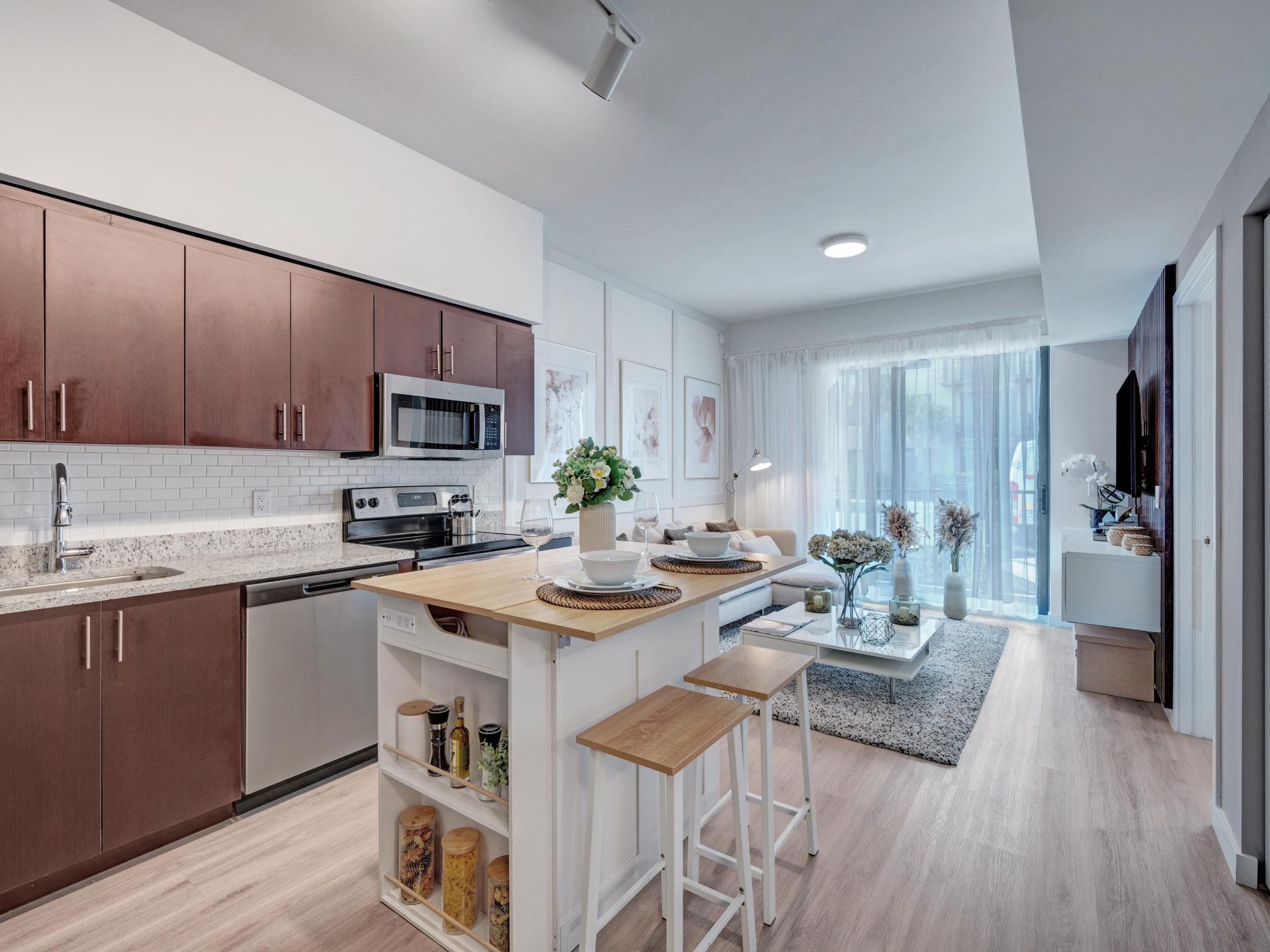 Modern kitchen and living area featuring stainless steel appliances, a center island with seating, and a cozy seating area with large windows letting in natural light.