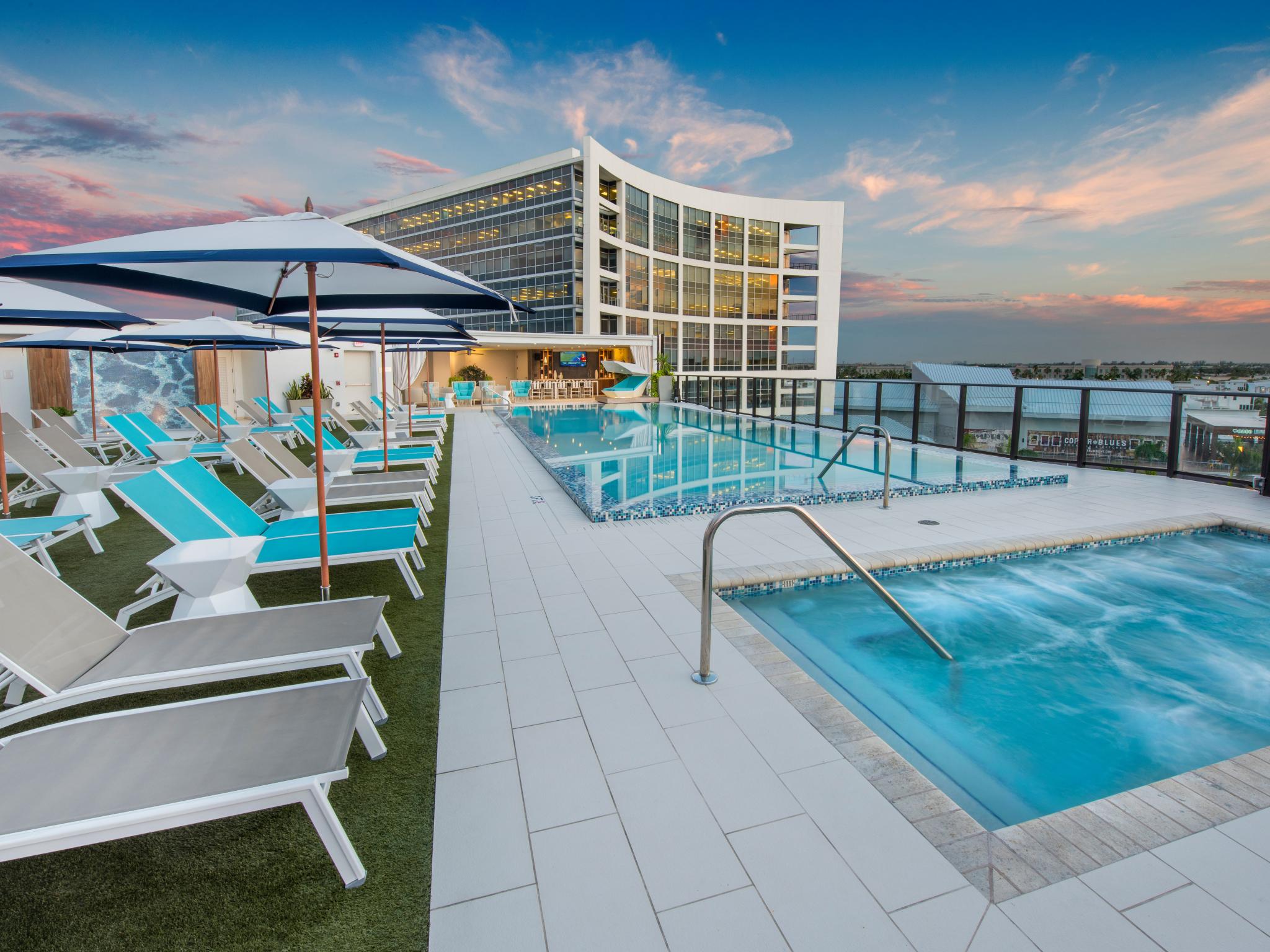 Rooftop pool at The Flats at City Place Luxury Apartments with modern lounge chairs, shaded cabanas, and stunning sunset views over the city skyline.
