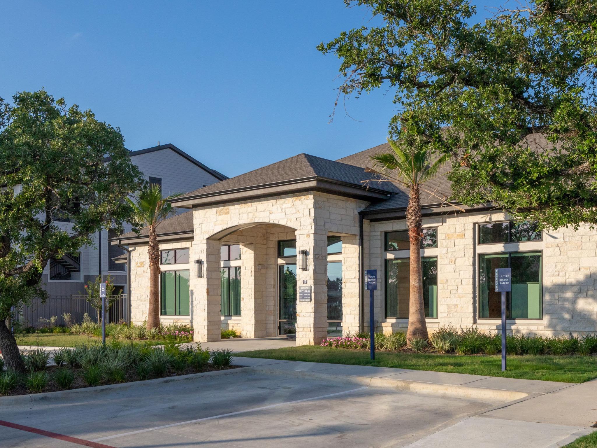 The leasing office exterior features a modern design with a stone facade, arched entryway, and lush landscaping, creating an inviting welcome to Vista At Town Green Luxury Apartments.