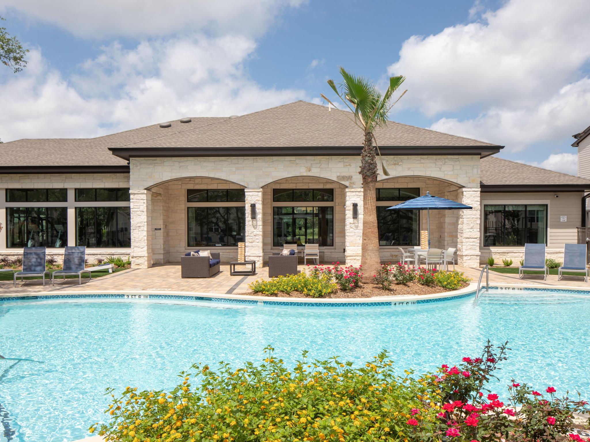 The resort-style pool area is surrounded by lounge chairs, lush landscaping, and an elegant clubhouse, offering a perfect retreat for relaxation and outdoor enjoyment.