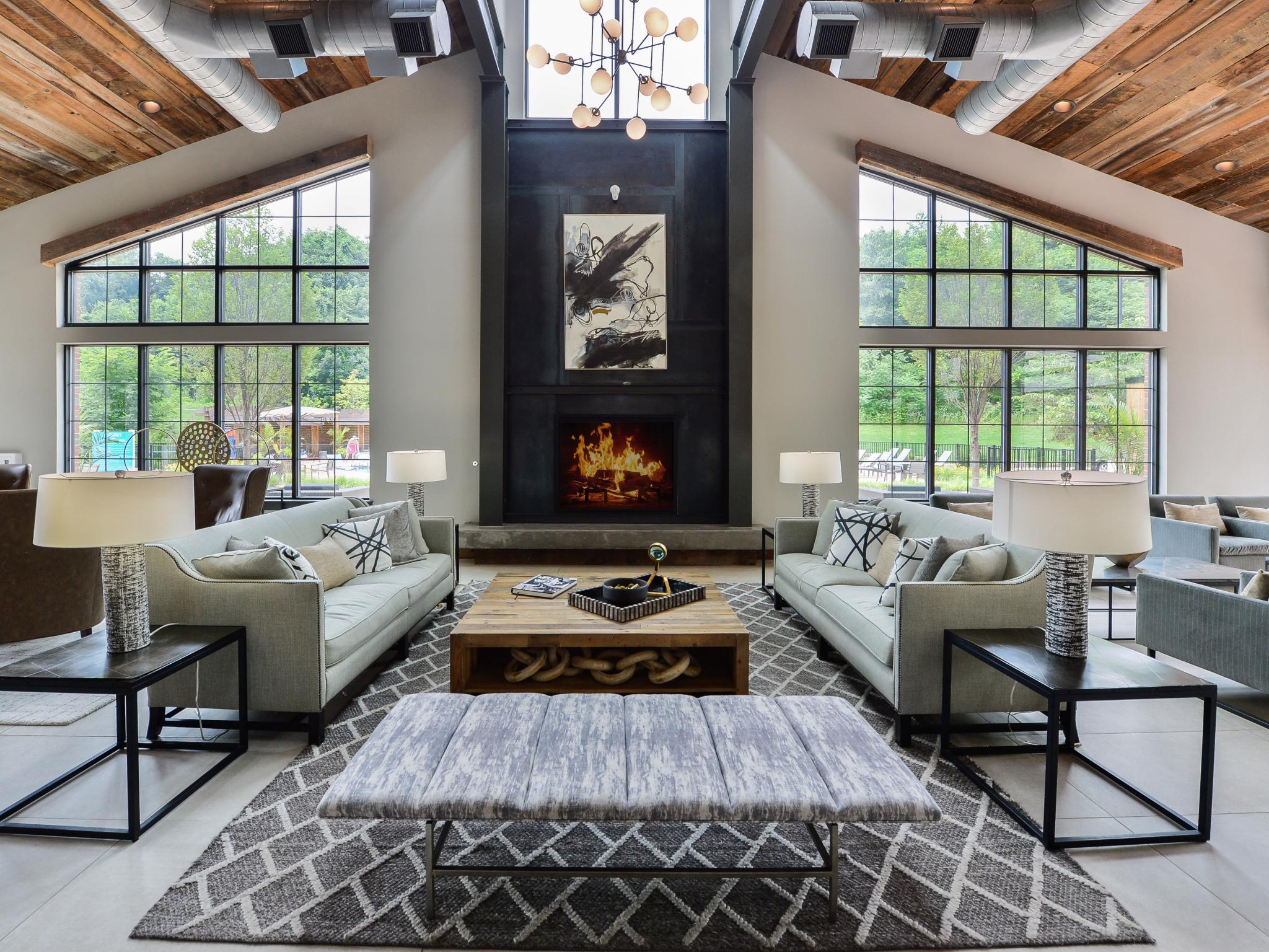 Elegant clubhouse interior with high ceilings, a warm fireplace, contemporary furnishings, and large windows showcasing serene outdoor views.