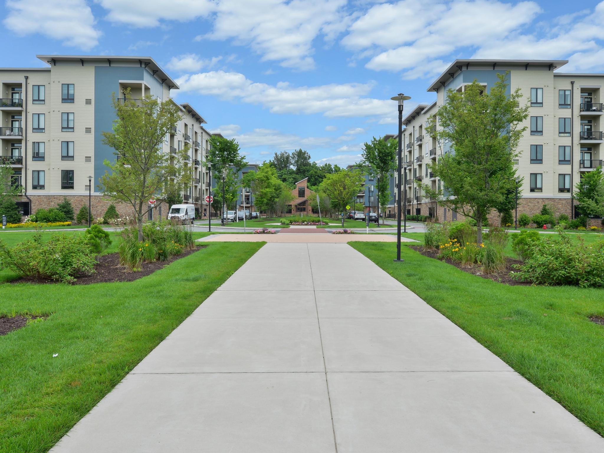 Expansive courtyard with beautifully landscaped gardens, wide walkways, and contemporary apartment buildings framing a scenic central green space.