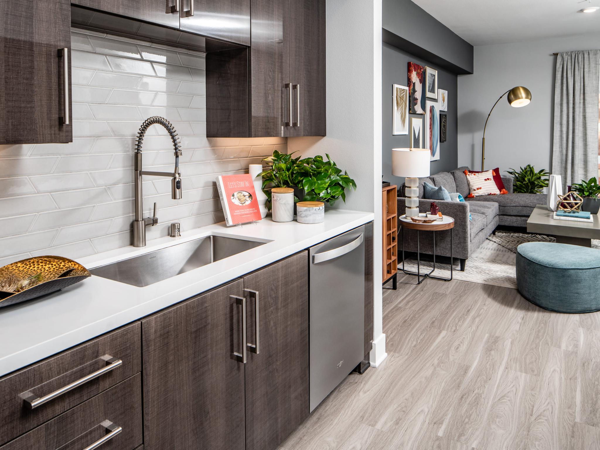 Modern kitchen at The Linden Luxury Apartments featuring sleek dark cabinetry, stainless steel appliances, and a stylish living area with contemporary decor.