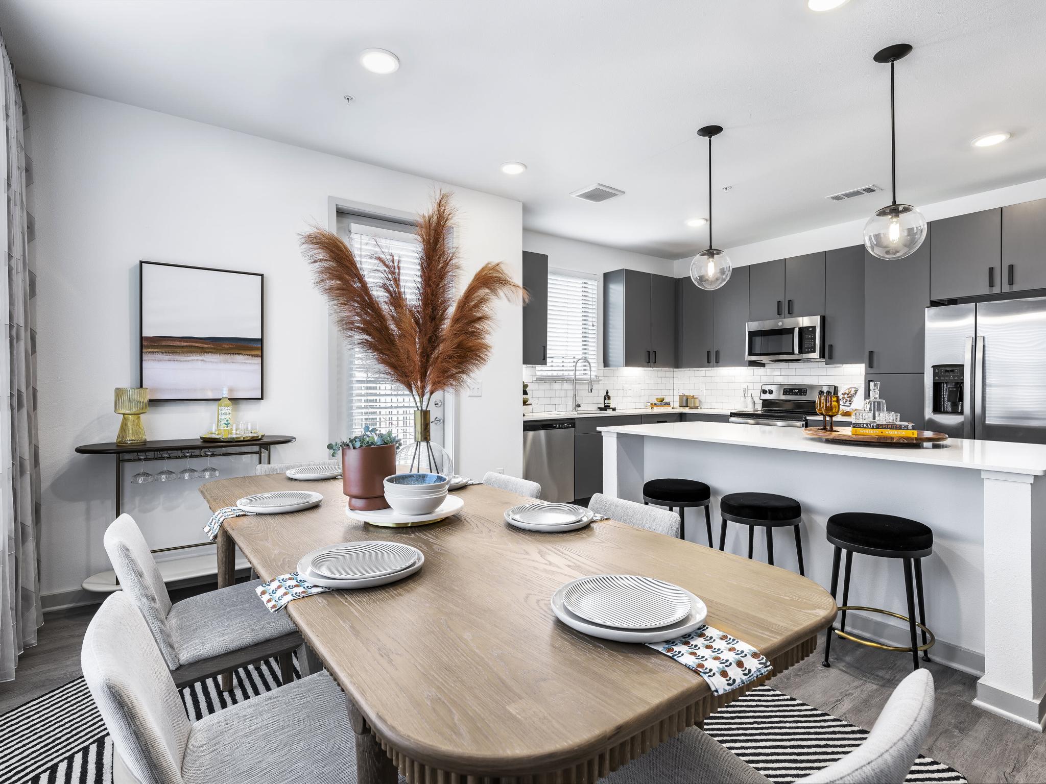 A stylish open-concept kitchen and dining area at The Warner Apartments, featuring sleek gray cabinetry, stainless steel appliances, and a beautifully set dining table with contemporary decor.