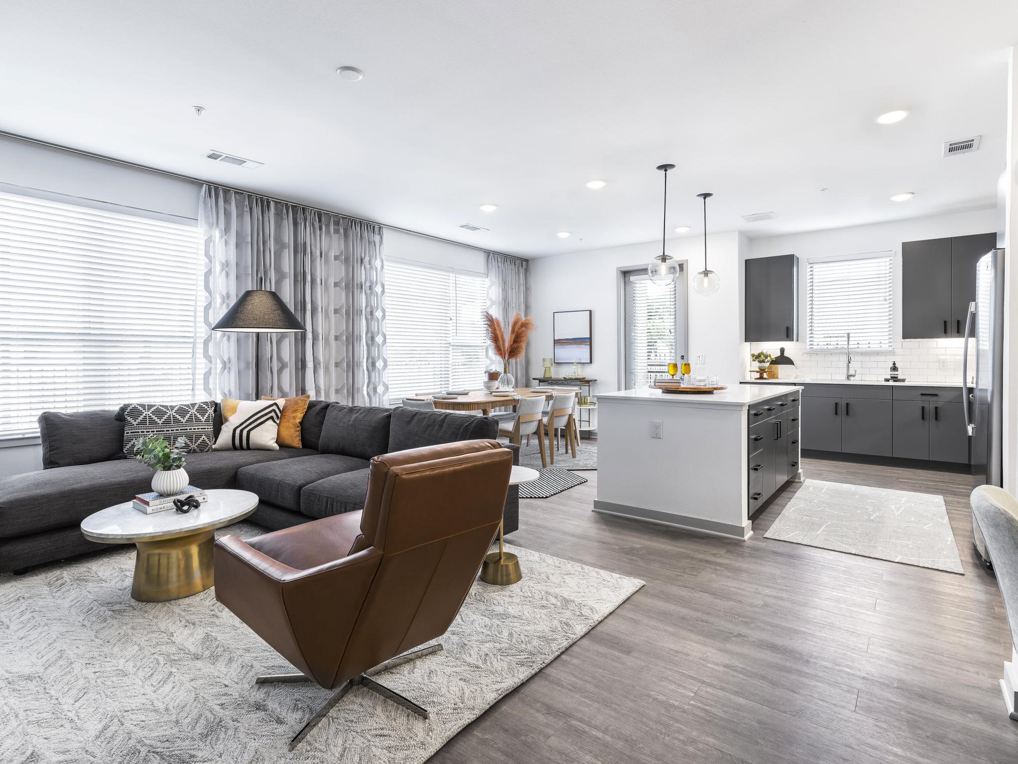 A luxurious open living space at The Warner Apartments, combining a cozy sectional sofa, elegant dining area, and a modern kitchen with pendant lighting and upscale finishes.