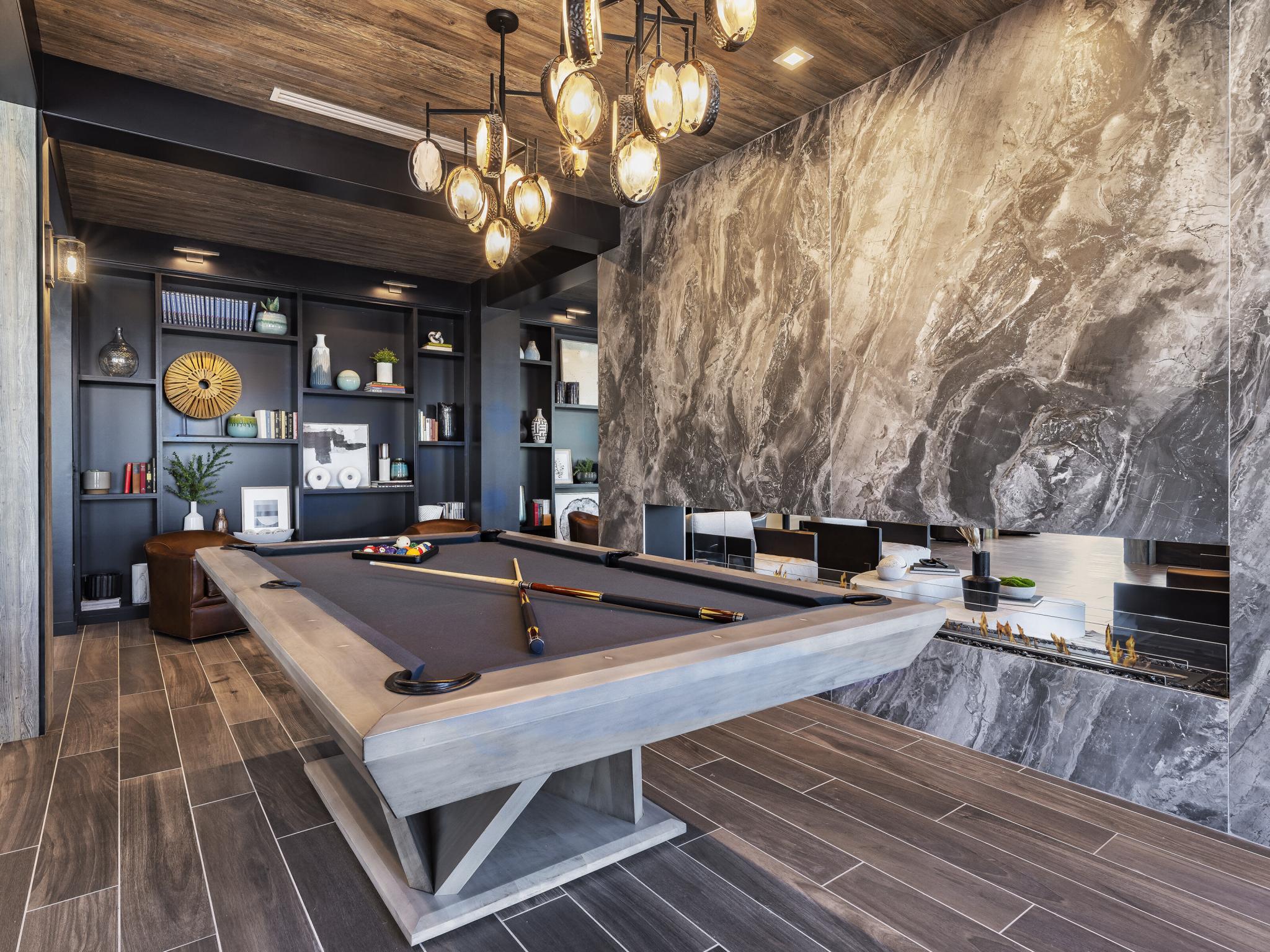 A sophisticated resident game room at The Warner Apartments, featuring a contemporary pool table, built-in bookshelves, and a sleek fireplace for a relaxing and social atmosphere.