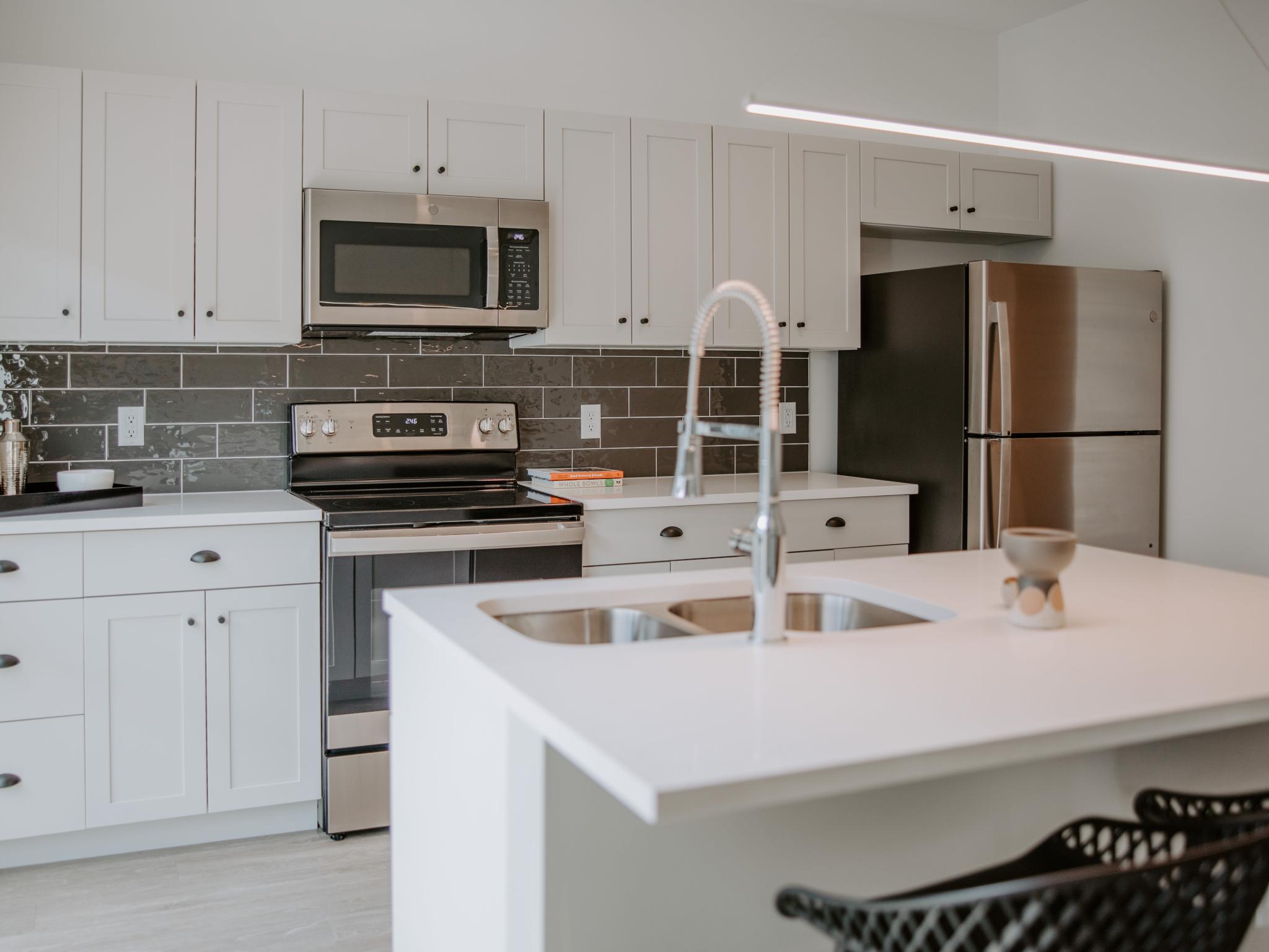 A modern kitchen in Industry Columbus Apartments featuring sleek white cabinetry, stainless steel appliances, and a stylish island with a dual sink and high-arc faucet.