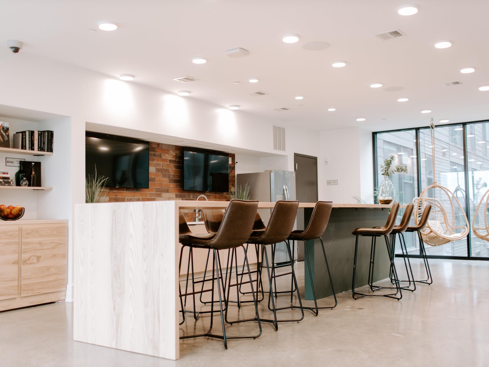 A spacious and well-lit community lounge in Industry Columbus Apartments, featuring high-top seating, hanging wicker chairs, and a kitchenette with modern finishes.