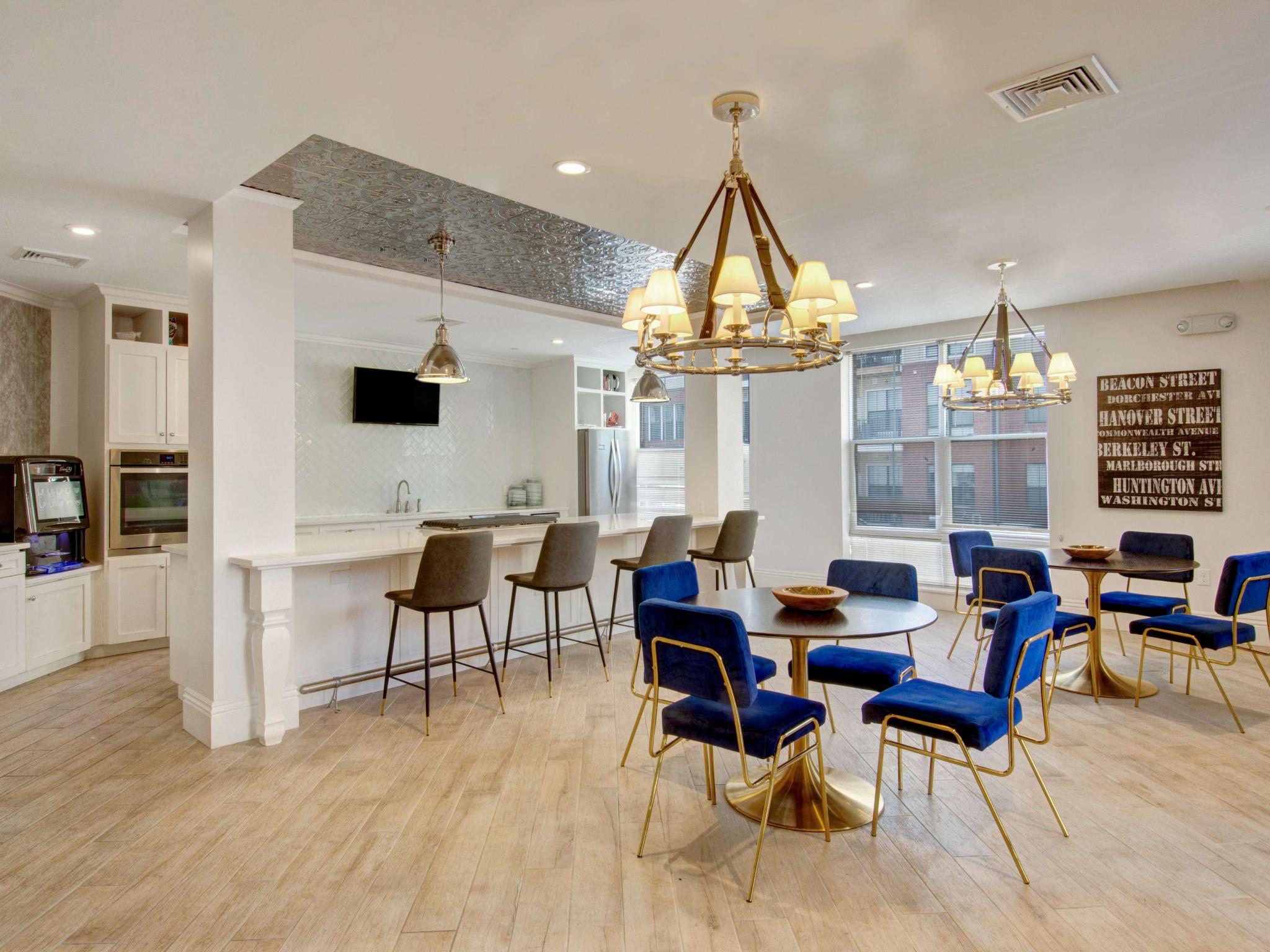 Modern community kitchen and dining space with pendant lighting, navy chairs, and light wood flooring.