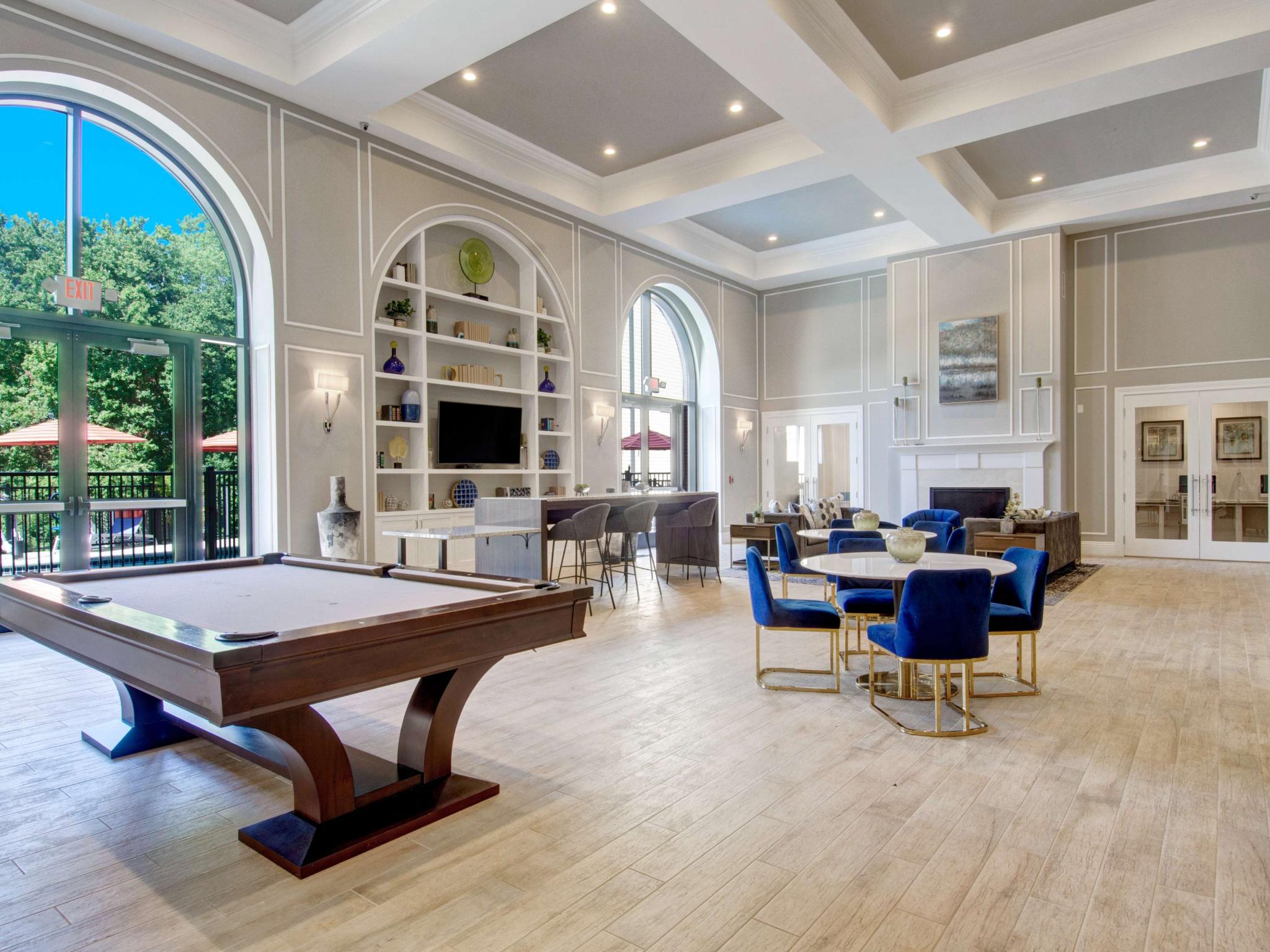 Spacious resident lounge featuring pool table, tall arched windows, and built-in shelving with decor.