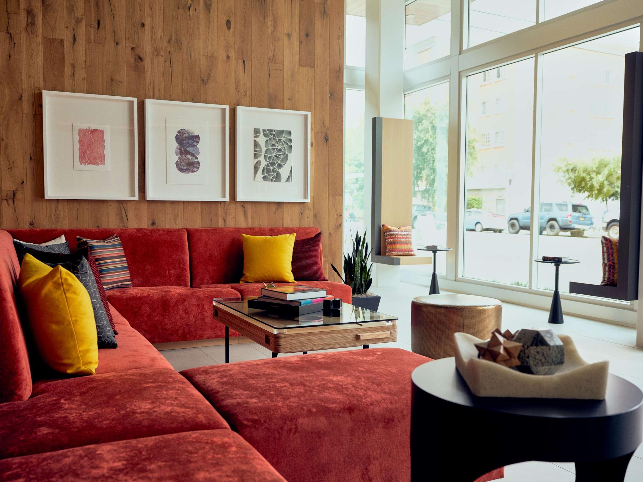 Contemporary resident lounge featuring a red sectional sofa, large windows, wood accent wall, and colorful artwork.