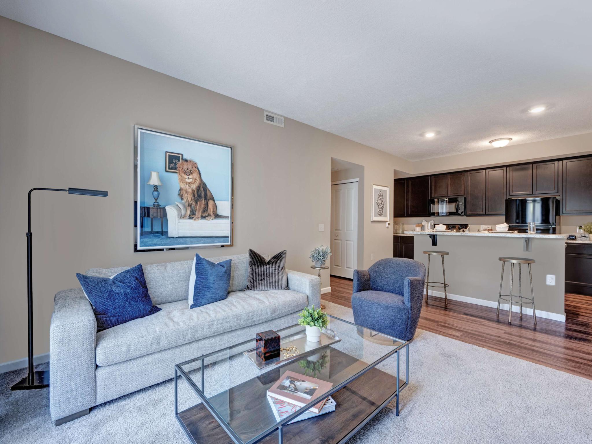 Open-concept living space with a contemporary sofa, large lion artwork, and a view into a kitchen with dark cabinetry and a breakfast bar.