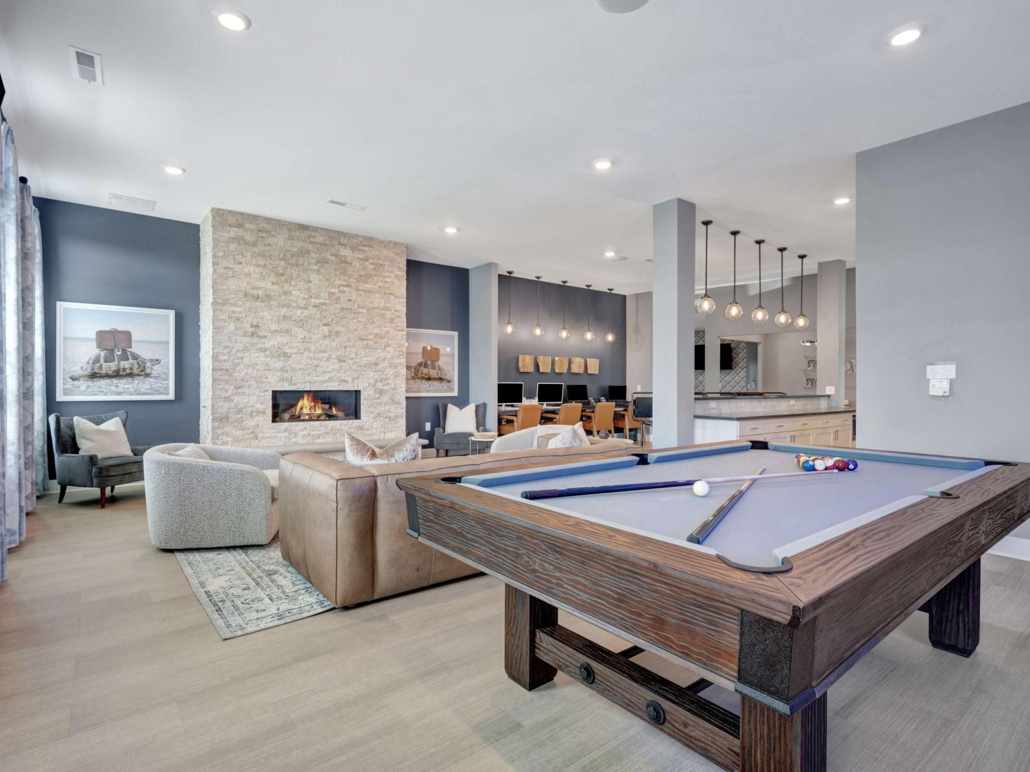 Amenity space with a pool table, resident lounge seating, and a business center, accented by modern lighting and a stone fireplace.