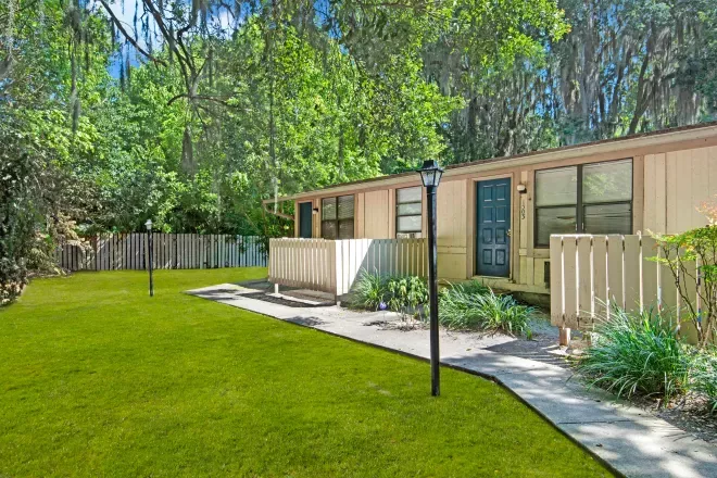 A charming apartment exterior with neatly maintained greenery and a fenced entrance.