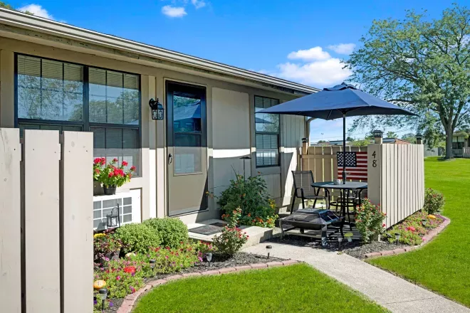 Private patio with umbrella and outdoor seating, surrounded by blooming flowers and well-manicured lawn outside apartment unit 48