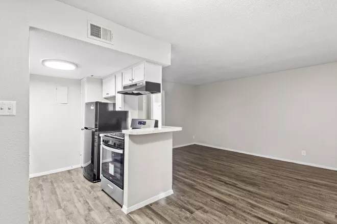 Modern apartment kitchen and open living room. White cabinets, stainless steel appliances, and wood flooring.
