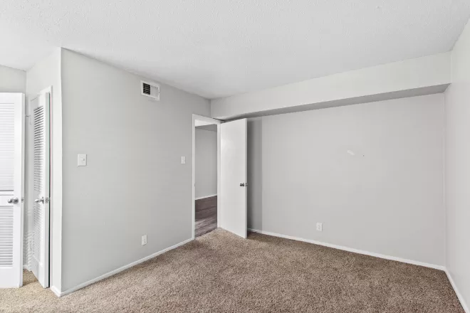 Unfurnished bedroom with light gray walls, brown carpet, and two open doorways.