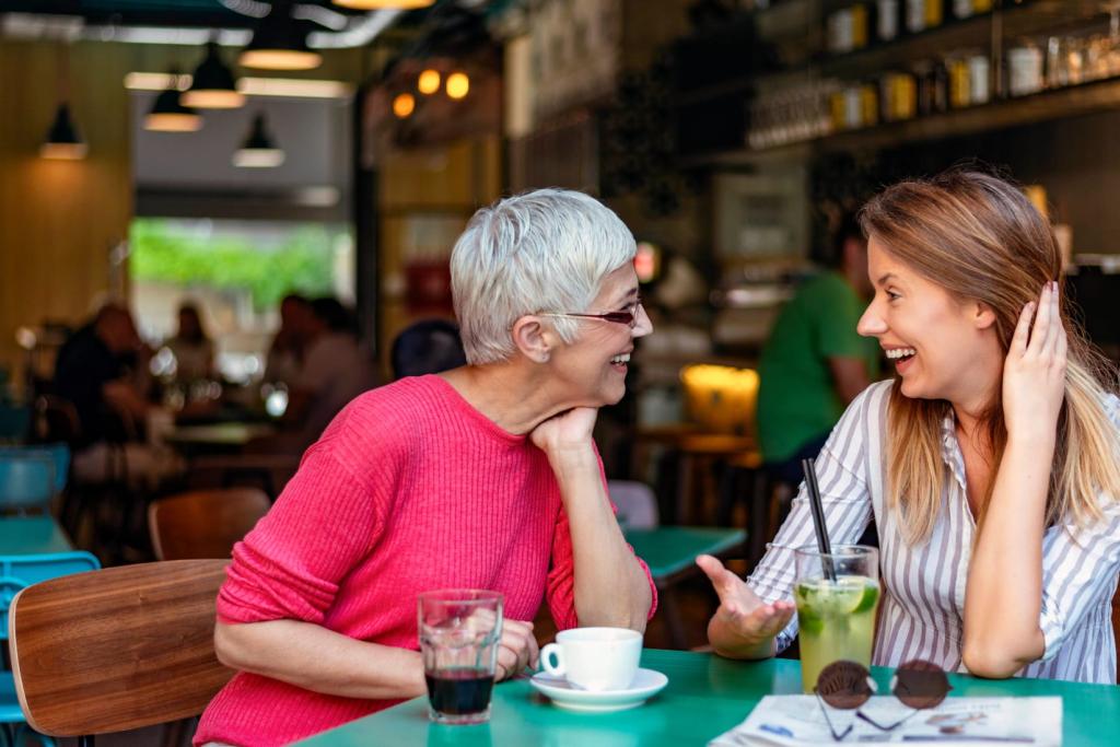 Two women, one older and one younger, smiling and engaged in a lively conversation at a café.